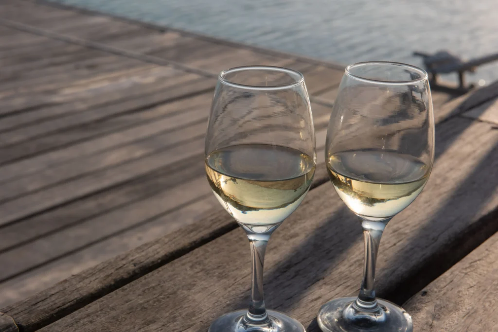 Dos copas de vino blanco servidas sobre una superficie de madera exterior en un día de verano.