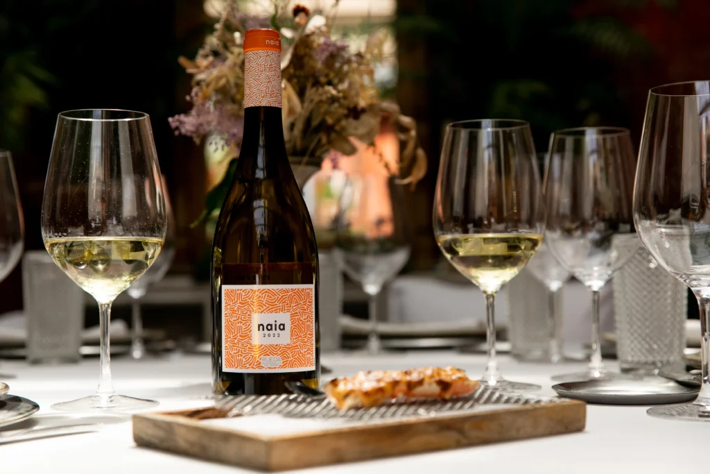 Botella de vino Naia junto a copas que contienen vino sobre una mesa. Esta imagen se utiliza para ilustrar una entrada sobre las diferencias entre un verdejo joven y un verdejo de guarda.