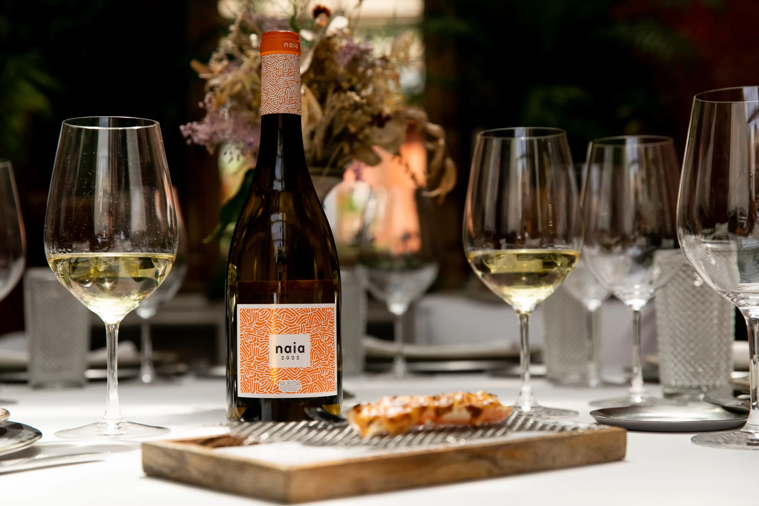 Botella de vino Naia junto a copas que contienen vino sobre una mesa. Esta imagen se utiliza para ilustrar una entrada sobre las diferencias entre un verdejo joven y un verdejo de guarda.